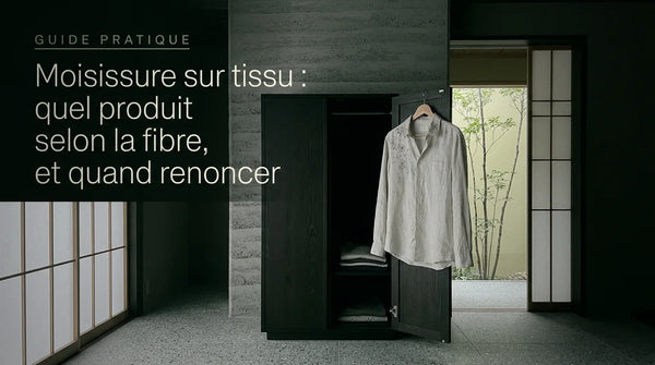 Chemise en coton clair sur un cintre devant une armoire ouverte, points gris de moisissure sur le col et l'épaule, lumière froide gris-vert